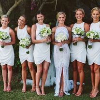 a group of women standing next to each other in white dresses and holding bouquets