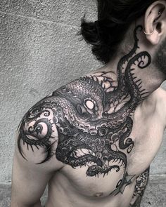 a man with an octopus tattoo on his chest and neck is standing in front of a wall