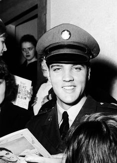 a black and white photo of a young man in uniform talking to people around him