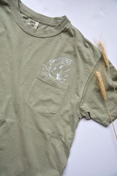 This rising trout pocket tee was created and produced in a small home office in Seattle, WA. This is a comfortable fishing tshirt with a high quality vinyl design above the pocket to make it look like the fish is coming through. This pocket tshirt is perfect for fishing, fly fishing men and women, nature lovers, lake lovers, and trout appreciators! It also make a perfect, unique gift for the fishing person in your life. They are UNISEX sizes so they tend to run true to size for men and runs a li Shirt Pocket Embroidery Men, Outdoor Relaxed Fit T-shirt With Pockets, Cotton T-shirt With Pockets For Outdoor, Khaki Crew Neck T-shirt With Pockets, Tshirt Pocket Design, Fishing Trip Outfit, Gifts For Fisherman, Fishing Clothes, Fly Fishing Shirts