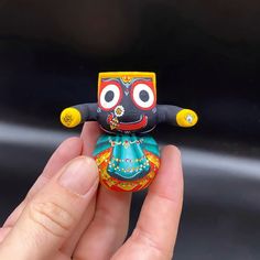 a hand holding a small colorful doll in it's right hand, with eyes wide open