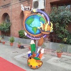 a colorful clock on the sidewalk in front of a brick building with plants and potted trees