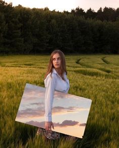 a woman standing in the middle of a field holding a painting