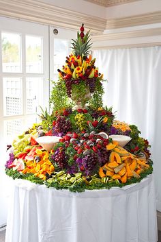 a large display of fruits and vegetables on a white table cloth in front of a window