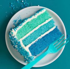 a piece of blue and green cake on a plate with a fork next to it