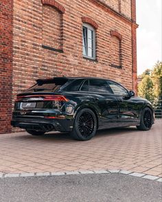 the rear end of a black car parked in front of a brick building with windows