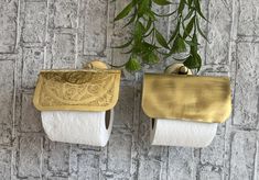 two gold and white toilet paper holders are hanging on the wall next to a plant