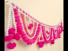 a pink and white wall hanging with tassels on it's sides, decorated with pom - poms