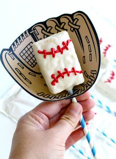 a hand holding a paper plate with baseball themed food on it and two straws in the background