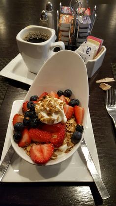 a white plate topped with fruit and yogurt next to a cup of coffee