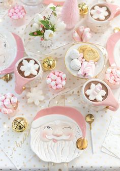 a table topped with plates and cups filled with candy covered santa clause cookies, marshmallows, and other candies