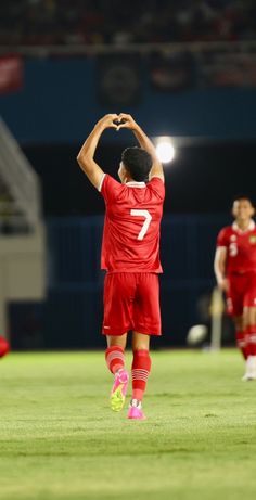 a soccer player is standing on the field with his arms in the air and one hand up above his head