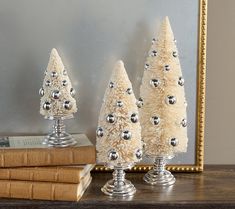 three small white christmas trees sitting on top of a wooden table next to a mirror