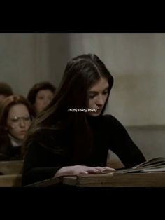 a woman sitting at a desk with an open book in front of her and people behind her