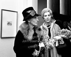 black and white photograph of two women in hats standing next to each other with flowers