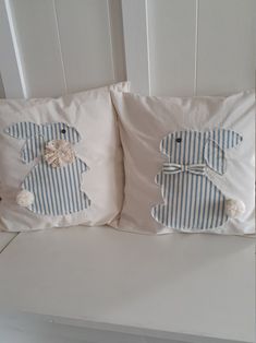 two decorative pillows on a white bench with blue and white striped pillow cases, one in the shape of a dog