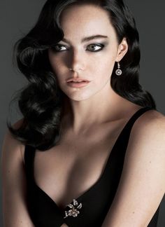 a woman with long hair wearing a black dress and diamond earrings, posing for the camera