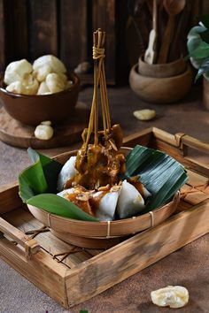 some food is in a wooden bowl on a tray with green leaves and other foods