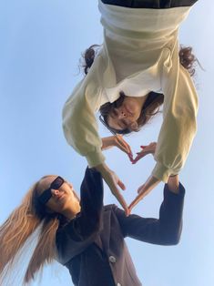 two young women are standing in the air making a heart shape with their hands and fingers