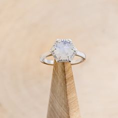 a white diamond ring sitting on top of a wooden stand