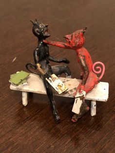 two small figurines sitting on top of a wooden table next to each other