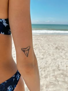 a woman with a small tattoo on her left arm and the ocean in the background