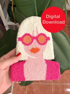 a hand holding up a knitted hat with pink and orange eyeglasses on it