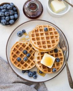 three waffles on a plate with butter and blueberries next to some syrup