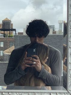 a man and woman taking a selfie in front of a mirror with buildings in the background