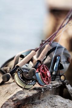 two fishing rods and reels are sitting on a rock near the water's edge