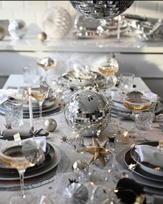 the table is set with silver and gold plates, glasses, and disco ball centerpieces