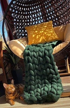 a cat laying on the ground in front of a chair and blanket that is made out of yarn