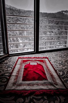 a red rug sitting on top of a black and white floor next to two windows