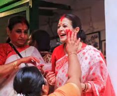 the woman is getting her face painted with red and white colors while others look on