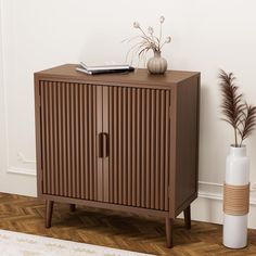 a brown cabinet next to a white vase with flowers on it and a bookcase in the corner