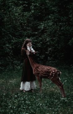 a woman standing next to a deer in a forest