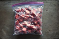 a plastic bag filled with strawberries sitting on top of a cement floor next to a wall