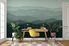 a desk with a yellow chair in front of a green mountain range wallpaper mural