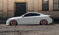 a white car parked in front of a brick building with red rims on it