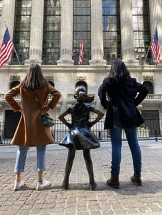 three women standing in front of a building with american flags on the wall street corner