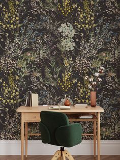 a desk with a green chair in front of a floral wallpaper