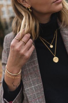 a woman wearing a black turtle neck sweater and gold bracelets, holding onto her jacket