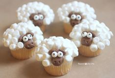 four cupcakes decorated with white frosting and brown sheep's eyes on them