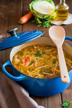 a blue pot filled with soup next to a wooden spoon on top of a table