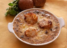 a white bowl filled with food next to two potatoes on top of a yellow table cloth