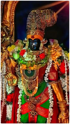 an idol is displayed in front of a gold statue with flowers and leaves on it