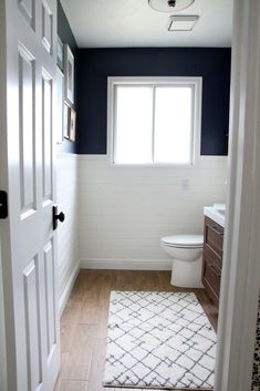 a white toilet sitting next to a window in a bathroom under a light fixture on a wooden floor