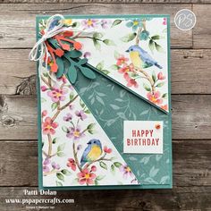 a handmade birthday card with colorful flowers and birds on it, sitting on top of a wooden table