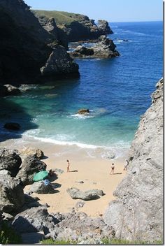 two people are standing on the beach near some rocks and water, while another person is walking in the distance