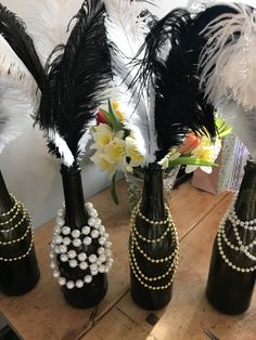 three black vases with pearls and feathers in them sitting on a table next to flowers